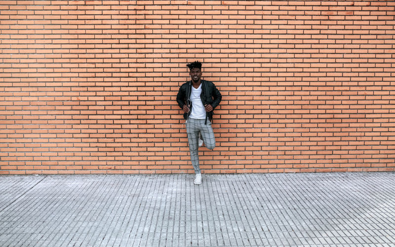 Mid adult man wearing leather jacket standing against brick wall