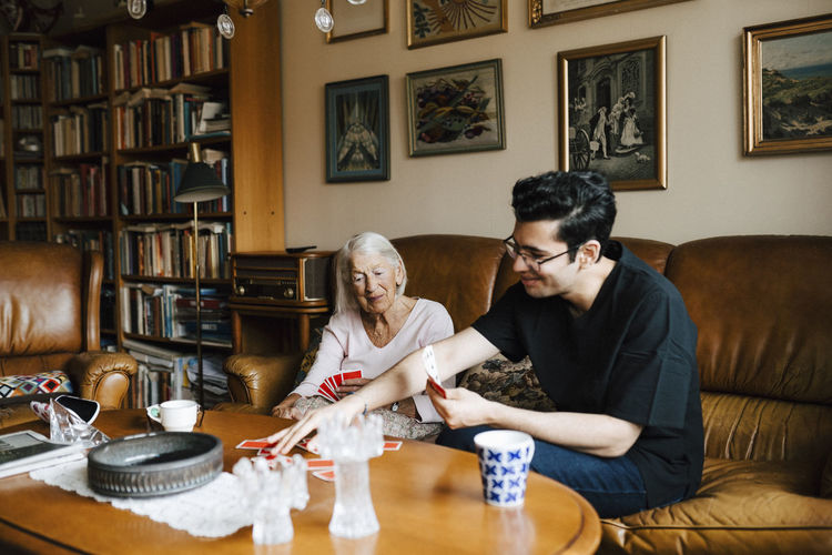 Senior woman and male nurse playing cards in living room at home