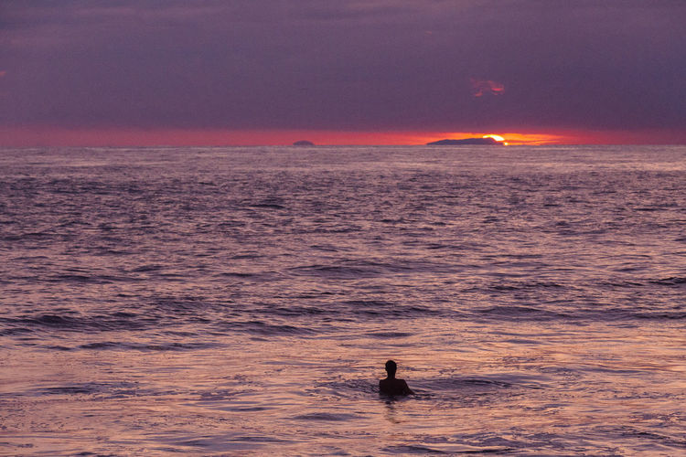 Silhouette swimming in sea against sky during sunset