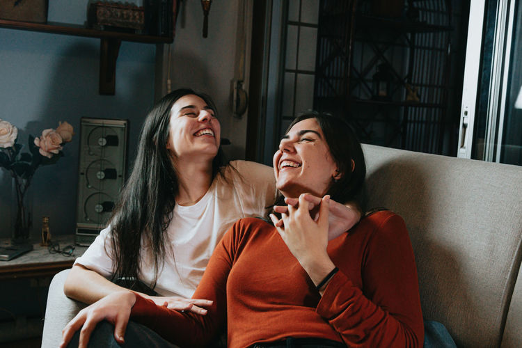 Women laughing while sitting on sofa at home