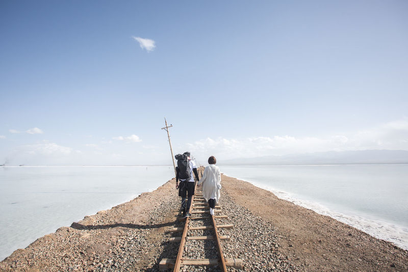 Rear view of couple walking on railroad track against sky