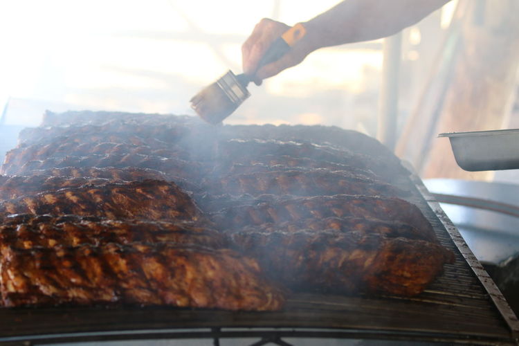Cropped image of vendor brushing ribs cooking on barbecue grill