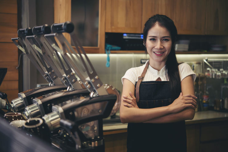 Portrait of smiling female barista with arms crossed standing at cafe