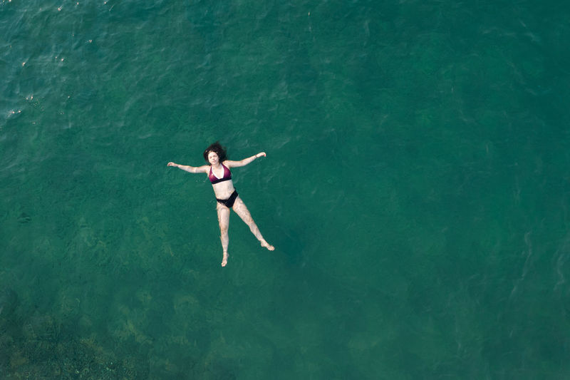 Woman with swimsuit floating and swimming in blue sea. overhead shot. aerial drone photograph