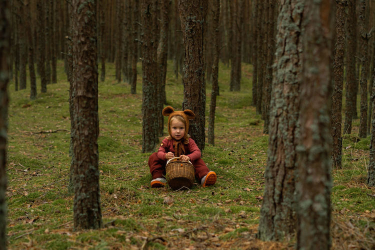 Toddler baby girl in bear bonnet sitting in the woods