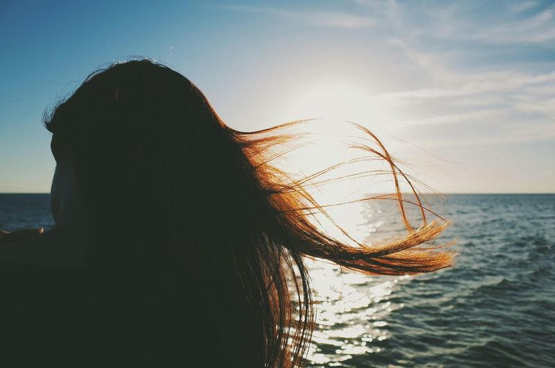 Close-up of a woman with hair blowing in wind against the sea