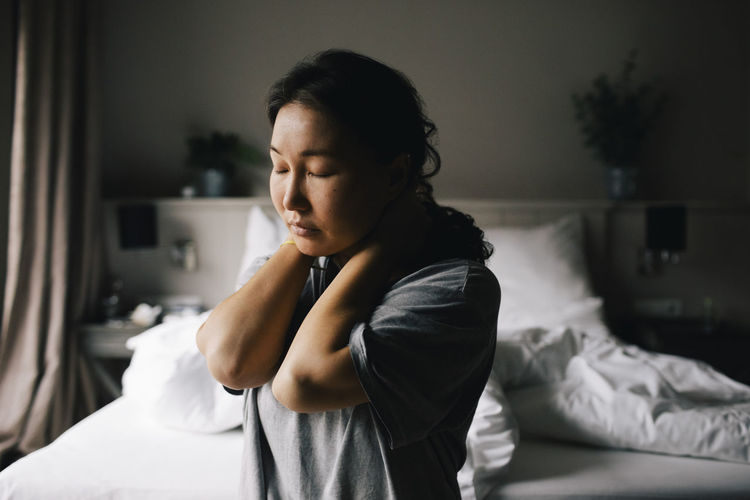 Depressed woman sitting with eyes closed against bed at home