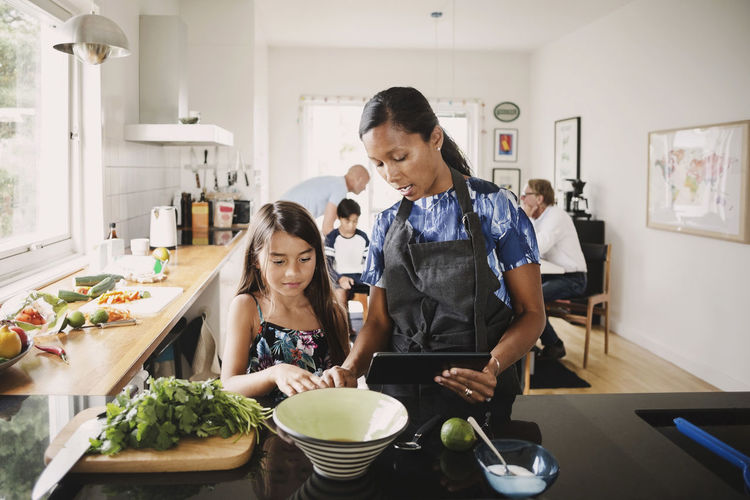 Mother and daughter using digital tablet while preparing food in kitchen