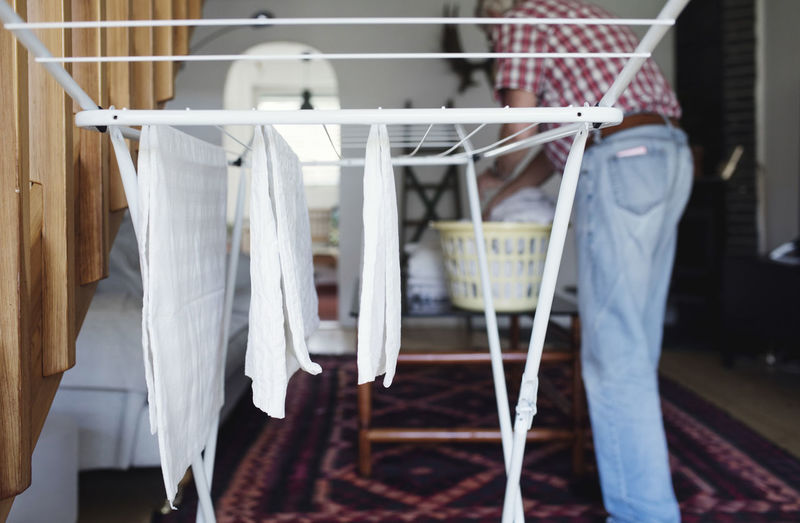 Clothes hanging on drying rack while senior man standing in background