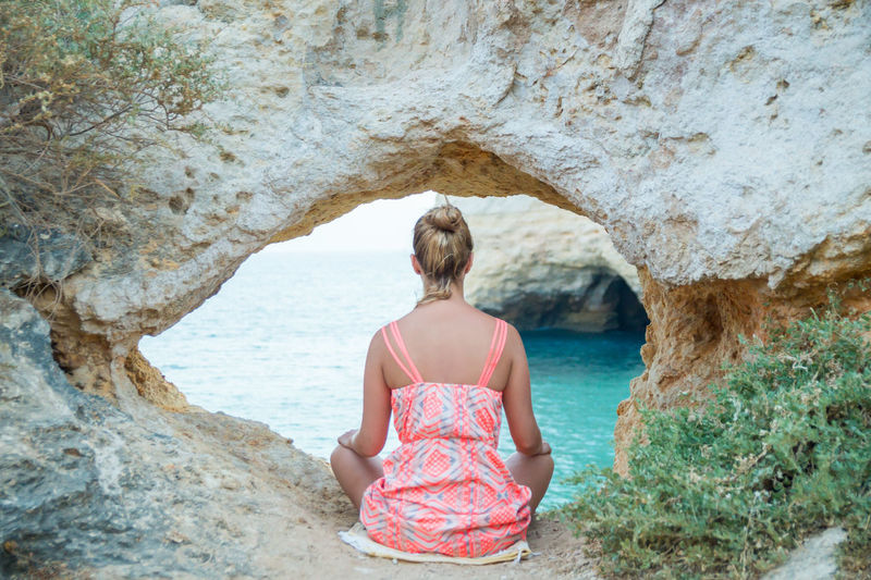 Rear view of woman looking at sea while sitting by rock