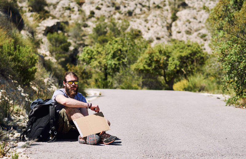 Portrait of young man holding blank cardboard while sitting on road
