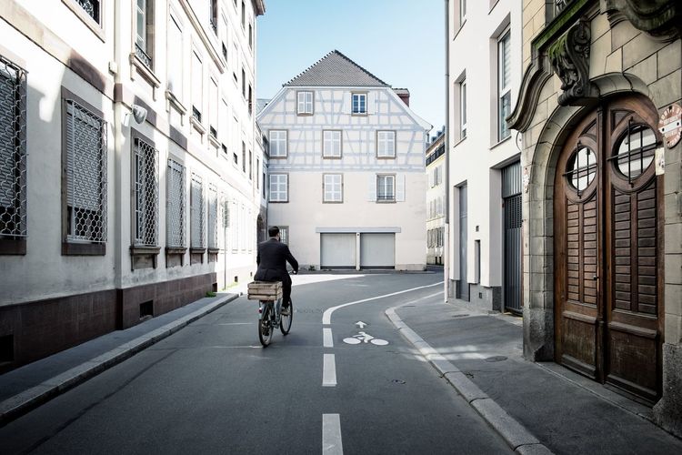 Rear view of man riding bicycle on road amidst buildings