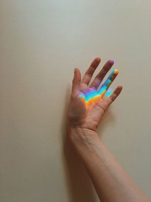 CLOSE-UP OF PERSON HAND HOLDING COLORED PENCILS AGAINST WALL