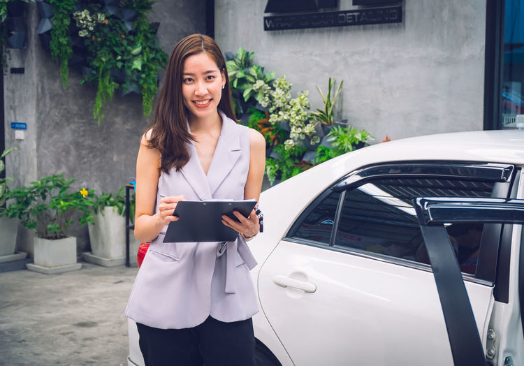 Portrait of smiling woman standing against car