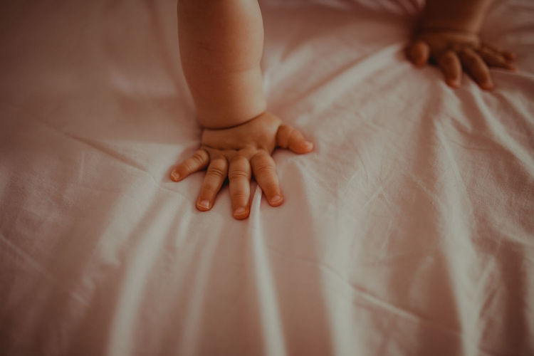 Low section of baby hand on bed