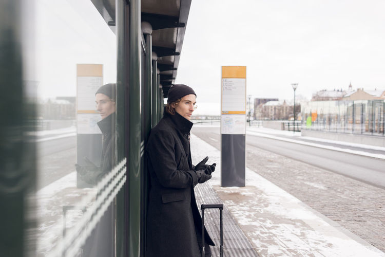 Young man waiting at bus stop in winter