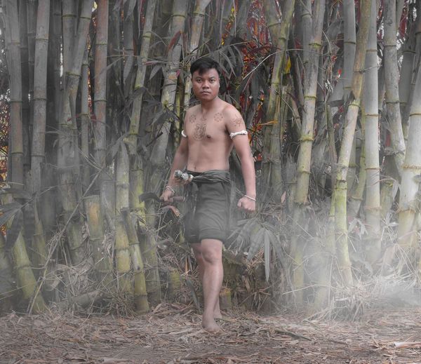 Portrait of shirtless young man standing by bamboo grooves in forest