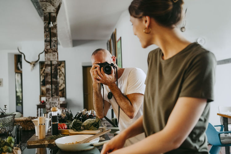 Male photographer taking picture of female chef cooking food in studio