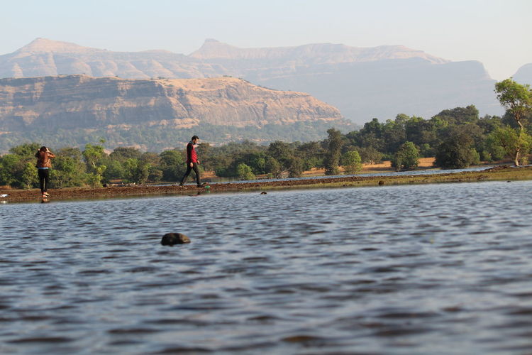 Man and woman walking on lakeshore against mountains at bhandardara