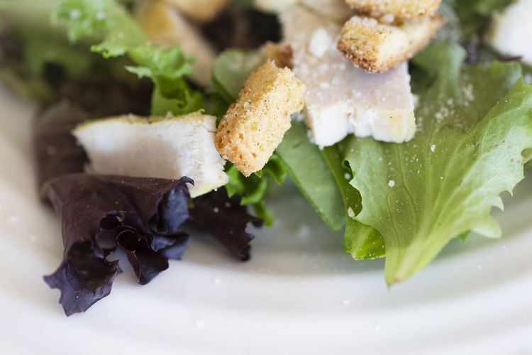 Close-up view of chicken pieces on salad with parmesan and croutons