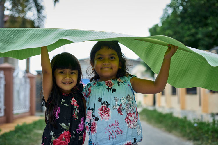 Portrait of smiling girls holding banana leaf outdoors