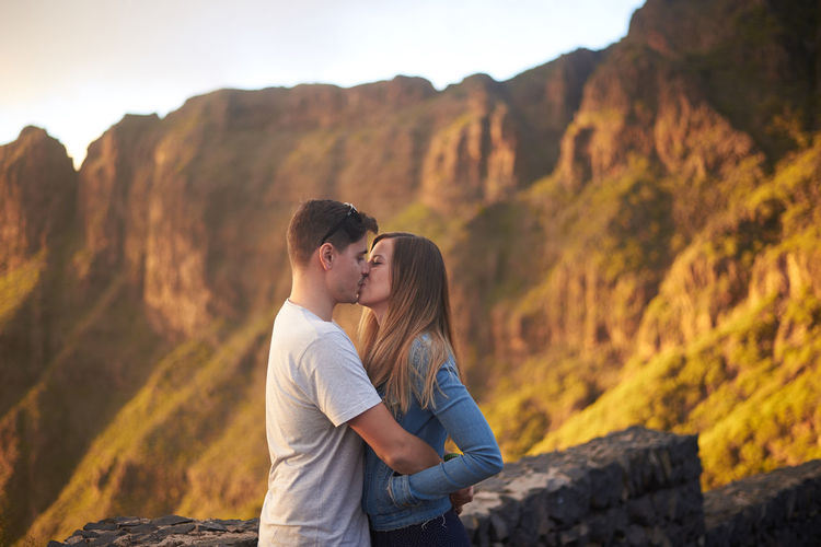 Side view of couple kissing against mountains