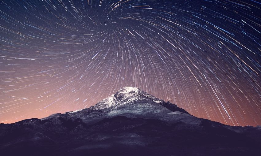 Low angle view of mountain against star trails against sky at night