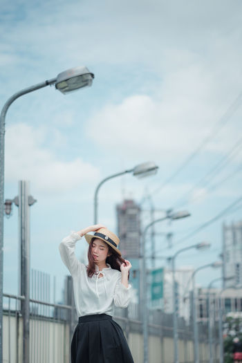 Young woman wearing hat while standing against railing and sky