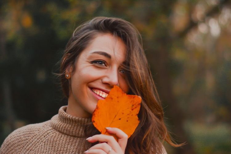 Close-up portrait of a smiling young woman with autumn leaves