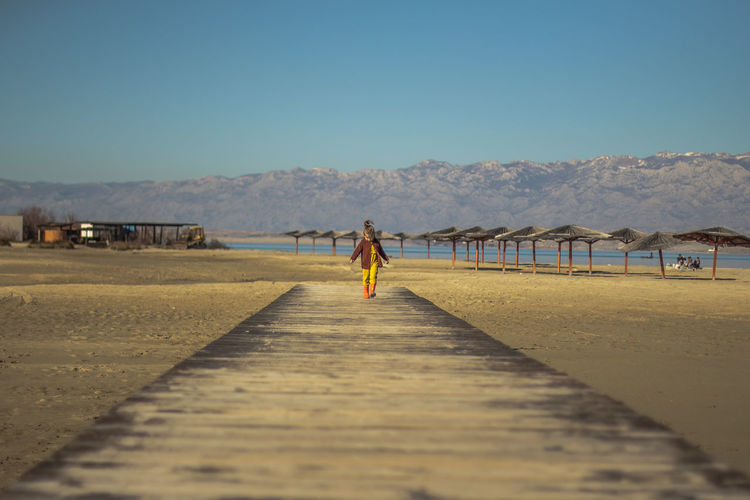 Mid distance view of girl walking on boardwalk at beach