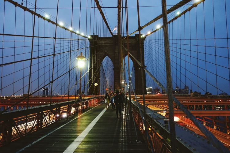 People on illuminated brooklyn bridge against sky at night