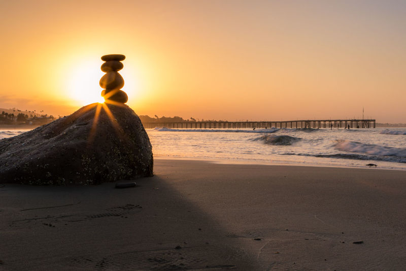 Stone stack on beach against sky during sunset 