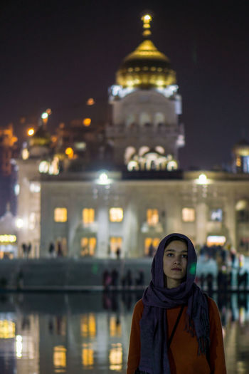 Portrait of woman standing against illuminated temple at night