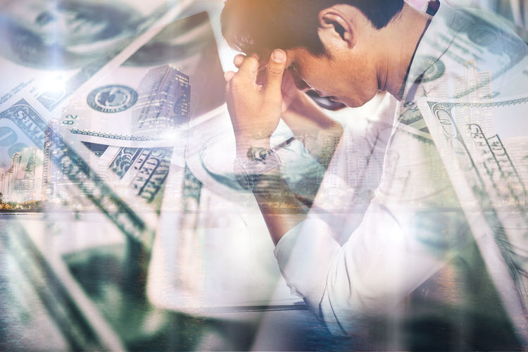 Digital composite image of depressed businessman surrounded by paper currencies