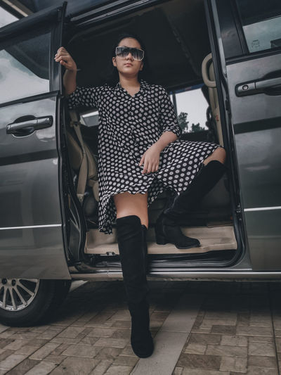 A girl wearing a polkadot dress, sun glasses and high boots sitting in a car 
