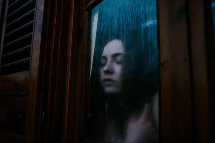 PORTRAIT OF WOMAN LOOKING THROUGH WINDOW