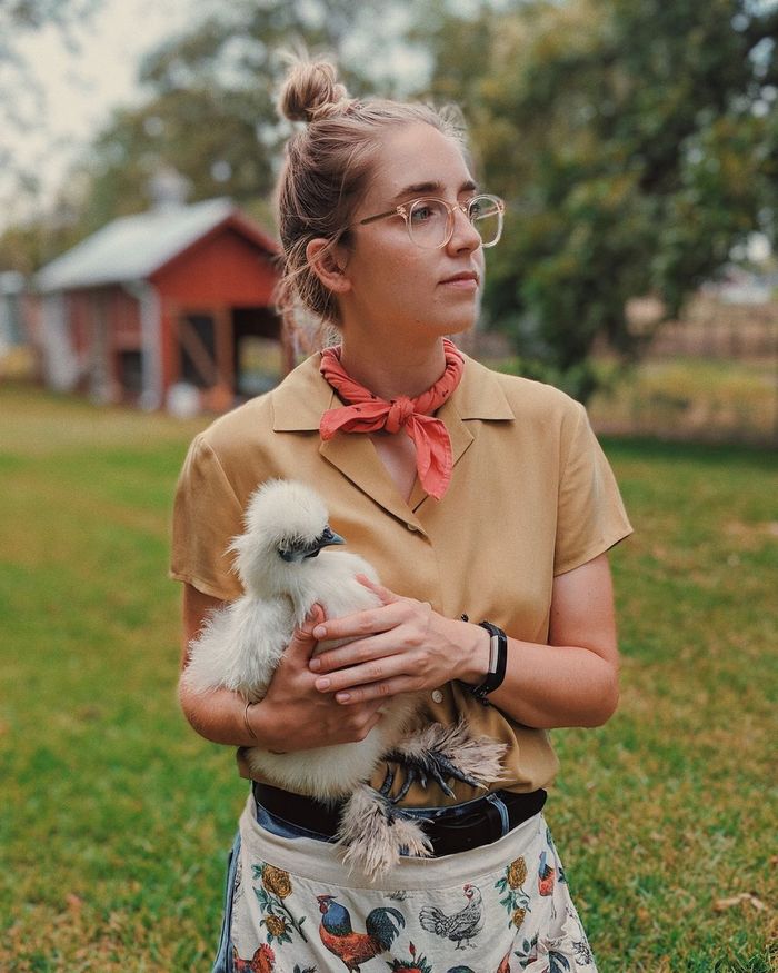 Young woman holding silkie while standing on grassy field