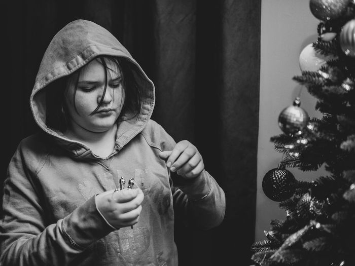 Girl wearing hooded shirt decorating christmas tree at home