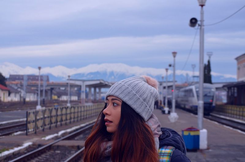 Close-up of woman looking away at railroad station platform against sky