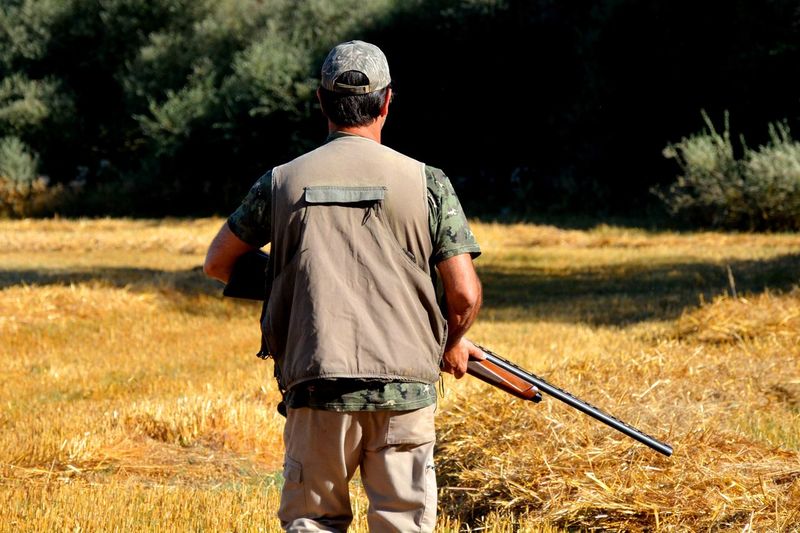 Rear view of man holding gun while standing on field