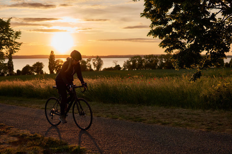 Woman riding bicycle on field against sky during sunset