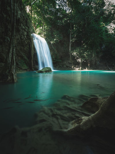Scenic waterfall with turquoise pond and sunbeam in forest. erawan falls, kanchanaburi, thailand.
