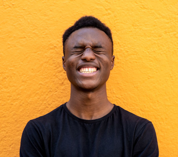 Smiling young man standing against yellow wall