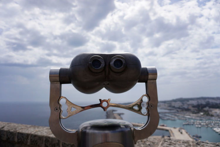 Close-up of coin-operated binoculars by sea against sky