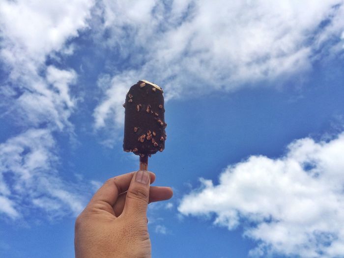 Close-up of hand holding ice cream against blue sky
