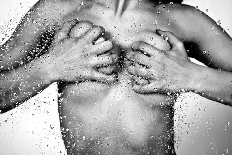 Midsection of sensuous woman squeezing boobs seen from wet glass in bathroom
