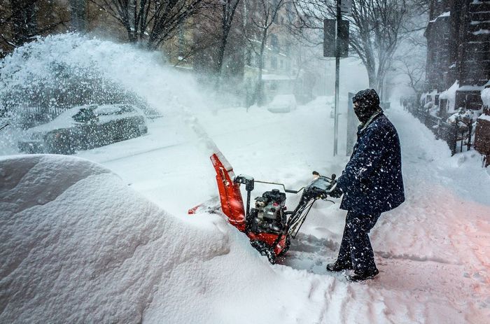 Side view of man holding snowblower during snowfall