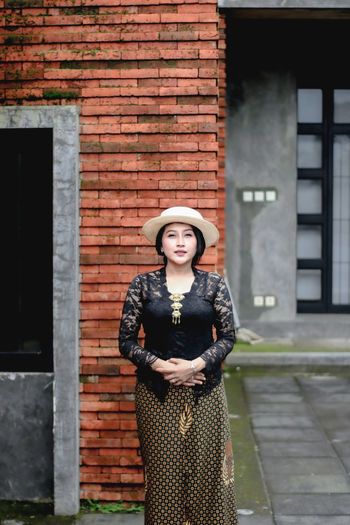 Portrait of a young woman standing against brick wall