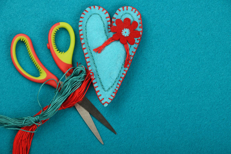Directly above view of scissors and threads by heart shape craft product on turquoise table