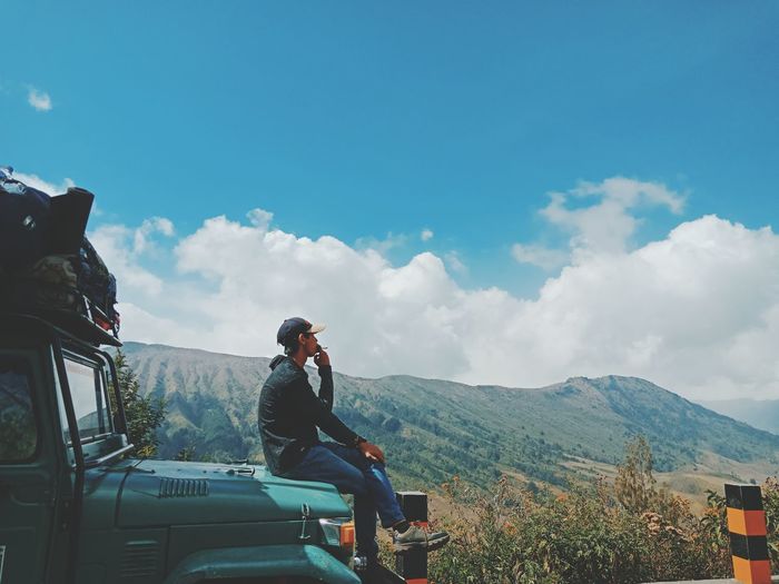 Man sitting on vehicle at mountain against sky